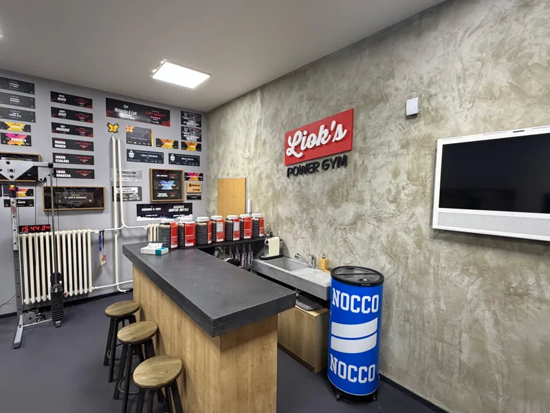 Bar s kávovarem a stoličkami pod cedulí Liok’s Power Gym